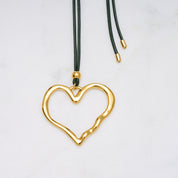Trendige goldene Herzkette mit Schnurband und dem Schriftzug ‚LOVE‘. Der 90er-Jahre-inspirierte Schmuck bietet eine verspielte und kraftvolle Note, mit flexibler Verschlussmöglichkeit durch Knoten oder Schlaufe.