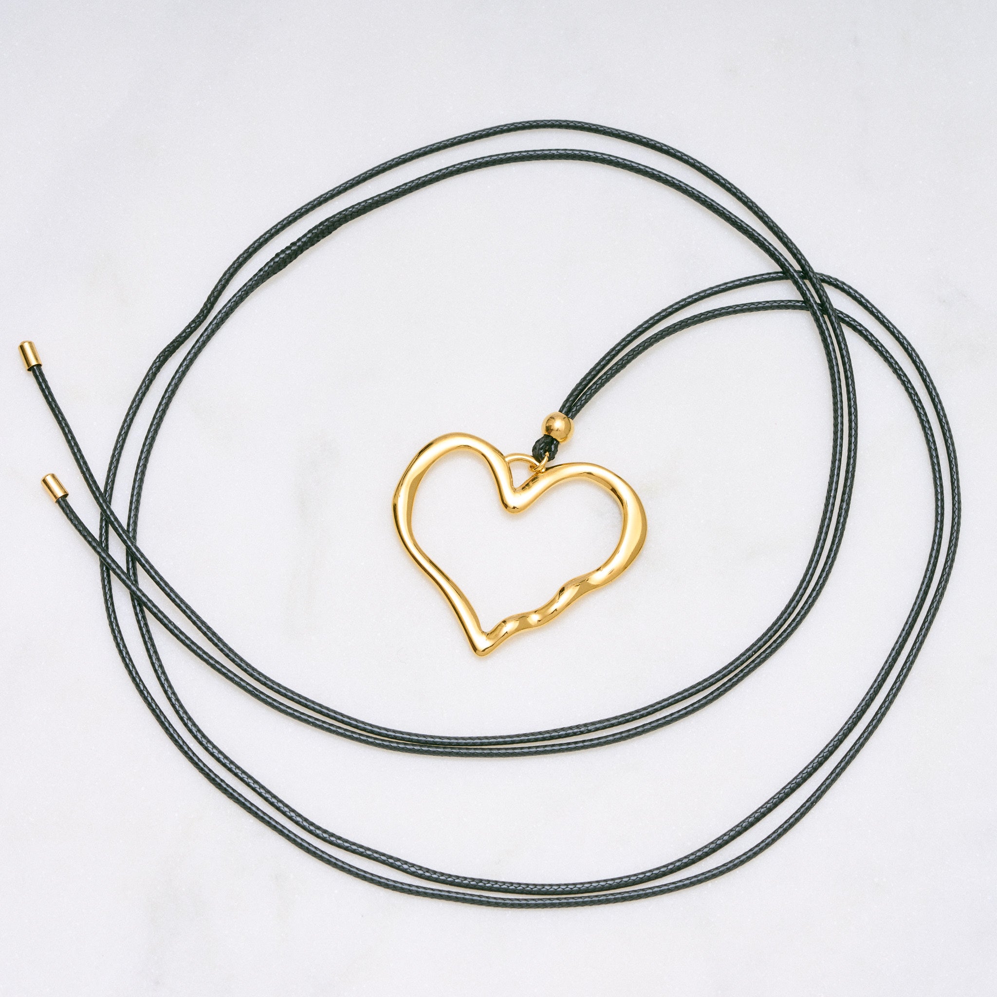 Trendige goldene Herzkette mit Schnurband und dem Schriftzug ‚LOVE‘. Der 90er-Jahre-inspirierte Schmuck bietet eine verspielte und kraftvolle Note, mit flexibler Verschlussmöglichkeit durch Knoten oder Schlaufe.