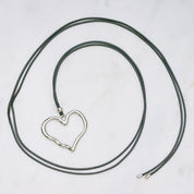Trendige silberne Herzkette mit Schnurband und dem Schriftzug ‚LOVE‘. Der 90er-Jahre-inspirierte Schmuck bietet eine verspielte und kraftvolle Note, mit flexibler Verschlussmöglichkeit durch Knoten oder Schlaufe.