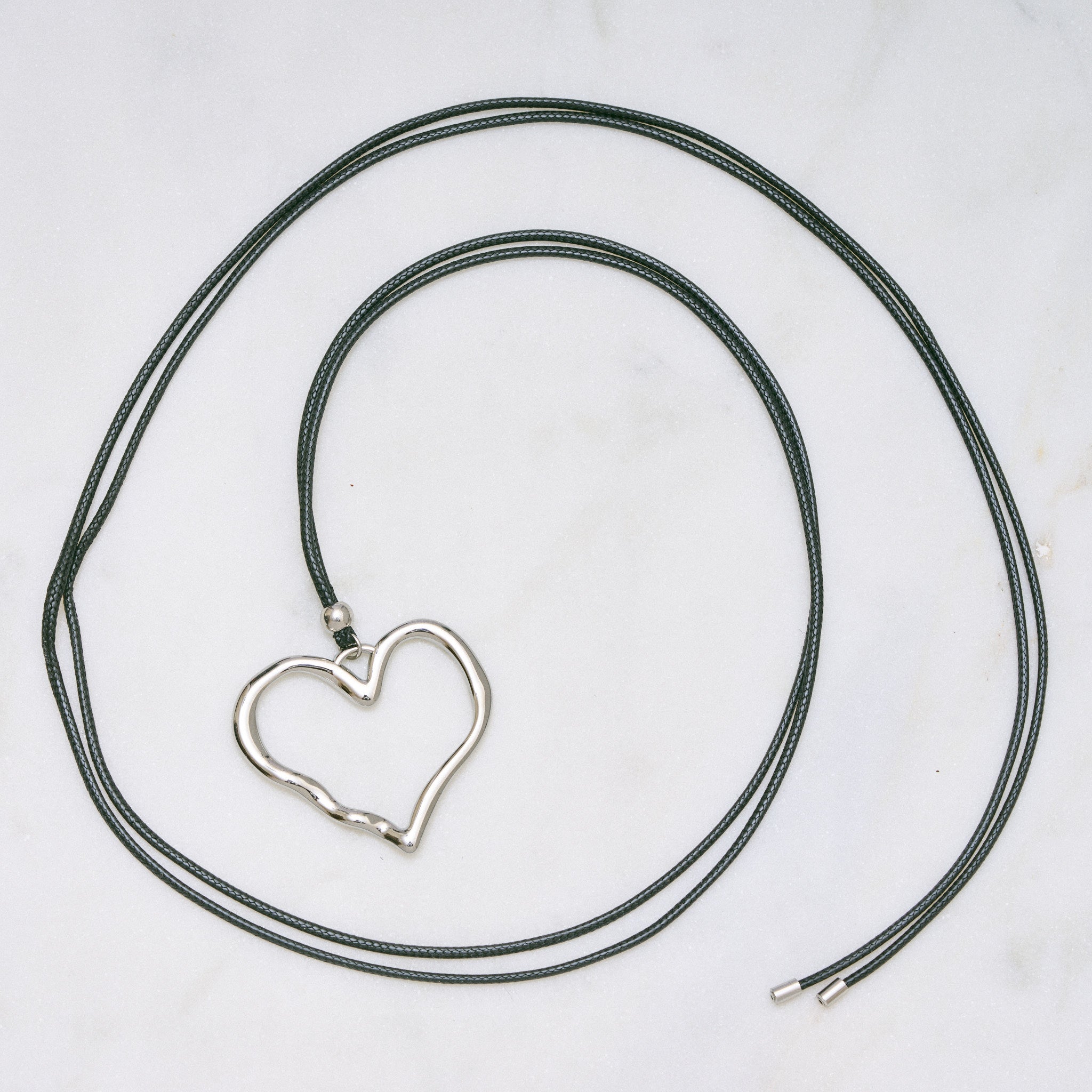 Trendige silberne Herzkette mit Schnurband und dem Schriftzug ‚LOVE‘. Der 90er-Jahre-inspirierte Schmuck bietet eine verspielte und kraftvolle Note, mit flexibler Verschlussmöglichkeit durch Knoten oder Schlaufe.