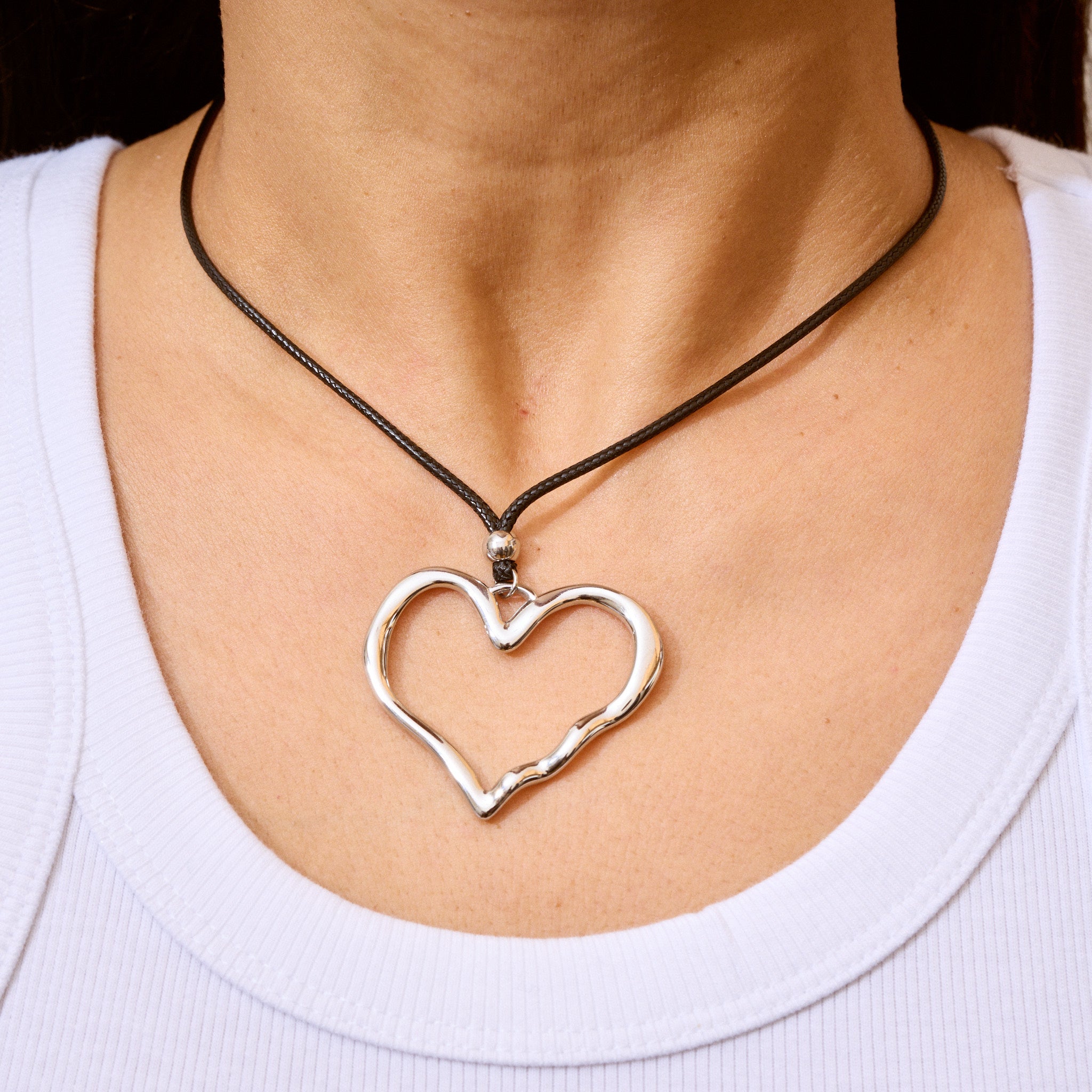 Trendige silberne Herzkette mit Schnurband und dem Schriftzug ‚LOVE‘. Der 90er-Jahre-inspirierte Schmuck bietet eine verspielte und kraftvolle Note, mit flexibler Verschlussmöglichkeit durch Knoten oder Schlaufe.