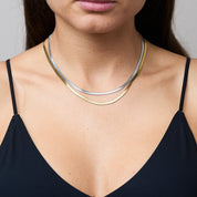 Zwei Snake Mini Ketten in Silber und Gold miteinander verbunden, die sich wie eine zarte Schlange um den Hals legen und im Licht glitzern. Die Bi-Color-Kombination betont den Trend-Look.