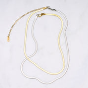 Zwei Snake Mini Ketten in Silber und Gold miteinander verbunden, die sich wie eine zarte Schlange um den Hals legen und im Licht glitzern. Die Bi-Color-Kombination betont den Trend-Look.
