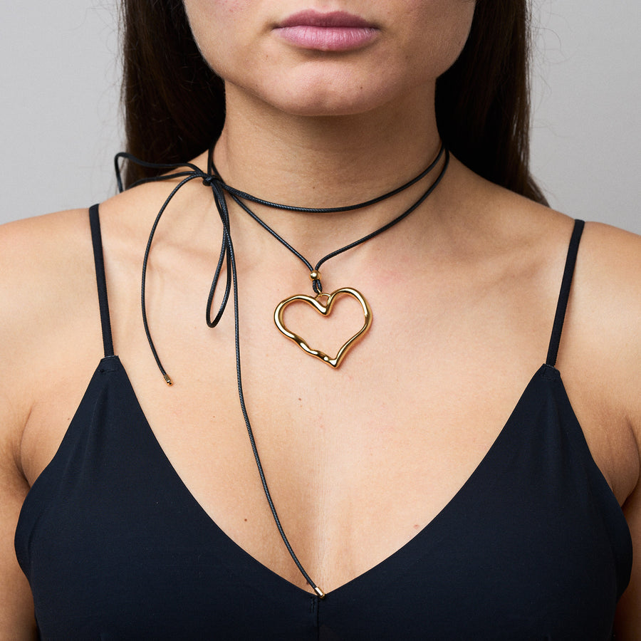 Trendige goldene Herzkette mit Schnurband und dem Schriftzug ‚LOVE‘. Der 90er-Jahre-inspirierte Schmuck bietet eine verspielte und kraftvolle Note, mit flexibler Verschlussmöglichkeit durch Knoten oder Schlaufe.